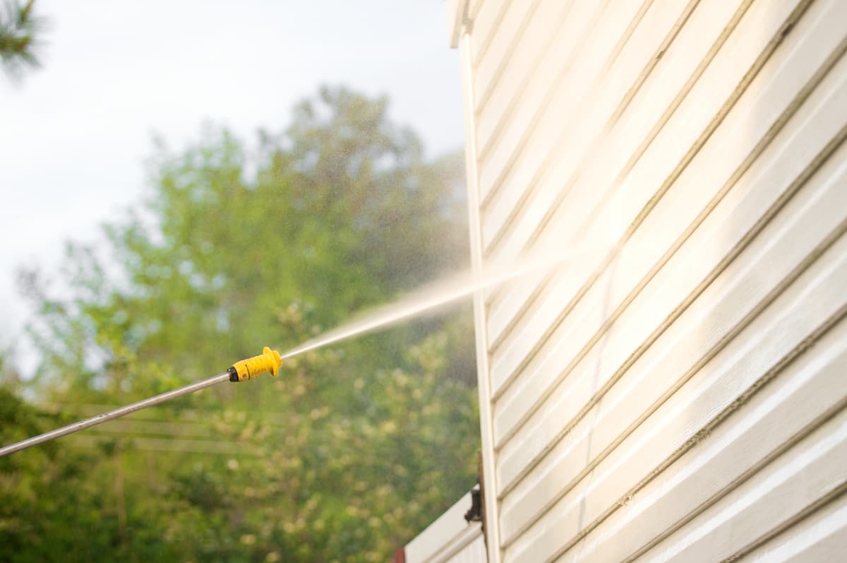 Pressure washer spraying cleaning solution on white house siding